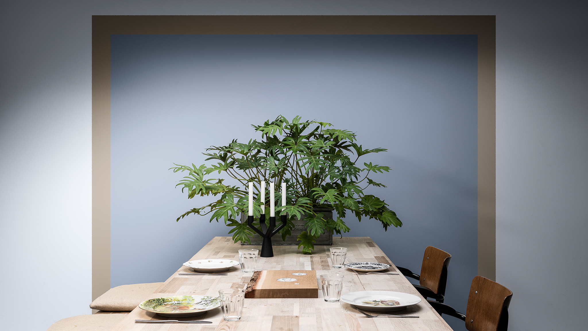 Eetkamer met een blauw vierkant met bruine rand op de muur geschilderd, met een tafel en plant Eetkamer met een blauw vierkant met bruine rand op de muur geschilderd, met een tafel en plant